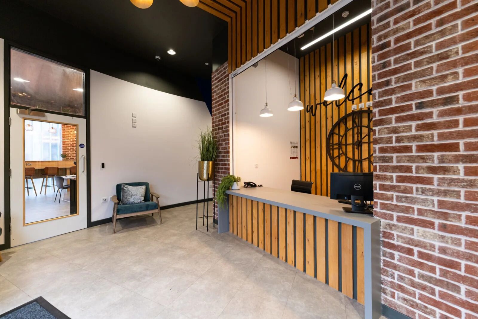 Una zona de recepción con un mostrador de madera, un sofá azul, una planta en maceta y un ventanal grande.