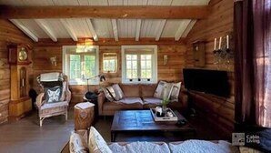 Interior d'una cabana de fusta amb un sofà, butaques, una taula de centre i una televisió.