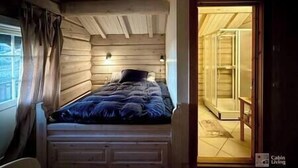 Un dormitori de cabana de fusta amb un llit, una tauleta de nit i una finestra amb cortines.