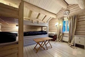 A cabin-style room with wooden walls and floors, bunk beds, a small table, and a window with curtains.