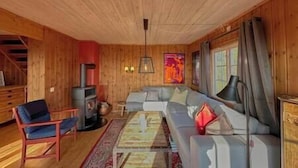 Interior de una cabaña con sofá, sillones, chimenea y un amplio ventanal.