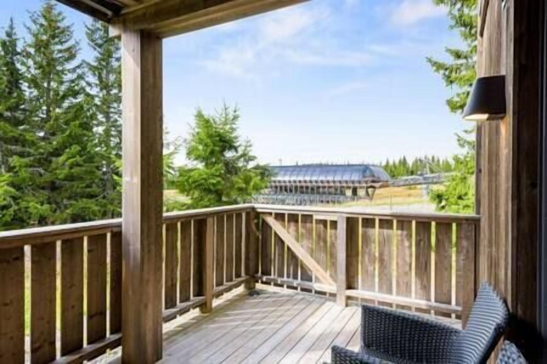 Une terrasse en bois offrant une vue sur un bâtiment doté d’un toit en pente et sur une clôture en arrière-plan.