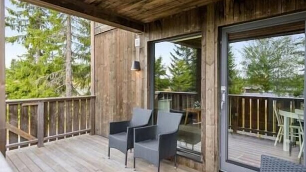 Un terrazzo in legno con due sedie e un tavolo, una porta vetrata che dà sull'esterno e una ringhiera in legno.