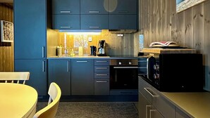 Una cucina moderna con mobili blu, soffitto in legno e zona pranzo con tavolo e sedie bianche.