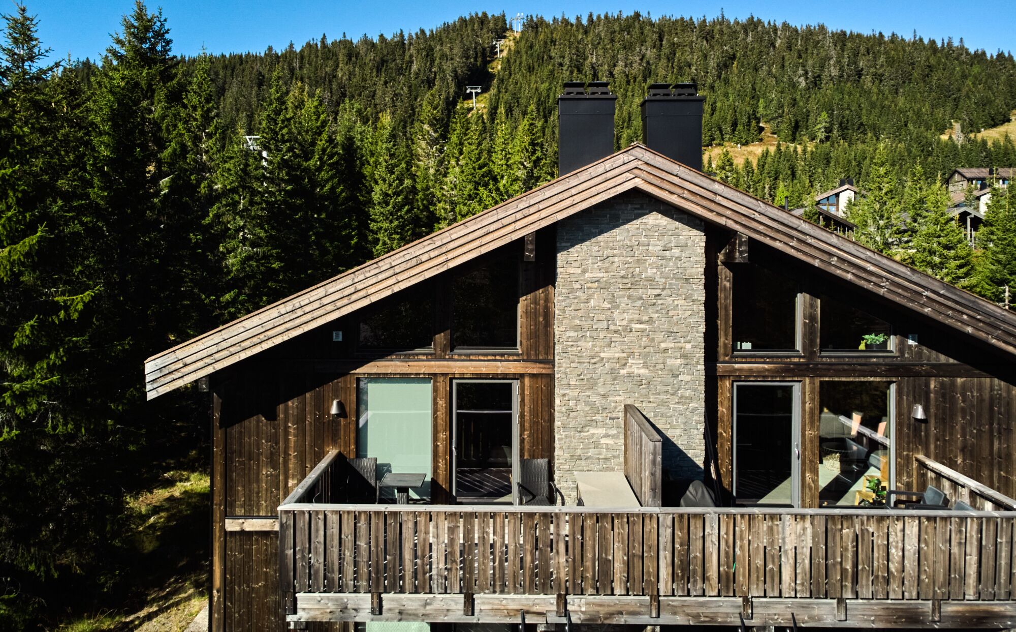 Eine Holzhütte mit Natursteinverkleidung, großen Fenstern und einem Balkon mit Blick auf ein bewaldetes Gebiet.