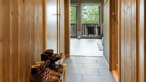 Un corridoio in legno con una fila di scarpe a sinistra e, sullo sfondo, un portico con ringhiera e un braciere.
