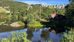 A lakeside cabin with a wooden exterior, surrounded by lush greenery and a clear sky. - Cozy apartment in a central location in Sirdal (Sirdal kommune)