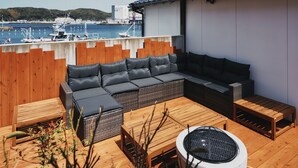 A wooden deck with a sofa, a table, and a fire pit. - THE RITOMARU IKI KAZENO OYADO (Iki)