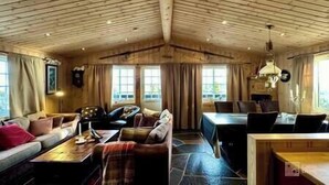 A cozy room with a wooden ceiling, a sofa, a table, and a dining area. - Cozy spacious cabin with sauna at Natrudstilen (Ringsaker)