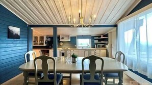 Een eetruimte met een houten tafel en stoelen, een kroonluchter en uitzicht op de keuken en woonkamer.