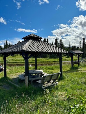 A rustic wooden pavilion with a table and benches, surrounded by lush greenery and a clear sky. - Large cabin Sjusjøen – XC ski in/out & lovely view (Ringsaker)
