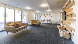 A modern office space with two sofas, a TV mounted on a wooden wall, and a large window providing natural light. - Student Only Stoneworks (Brighton)