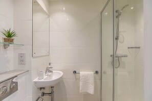 A modern bathroom with a glass-enclosed shower, a white sink, and a small shelf with a plant. - Student Only Stoneworks (Brighton)