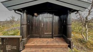 Una cabaña con revestimiento de madera oscura, una puerta principal y un conjunto de escalones de madera que conducen a la entrada.