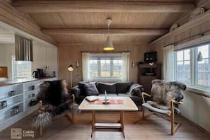 Cozy cabin-style room with a warm atmosphere, featuring a sofa, chair, and table with a lamp.