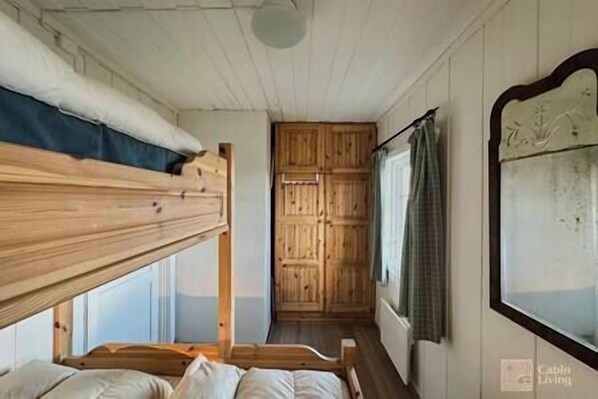 A bunk bed room with a wooden wardrobe and a window with curtains.