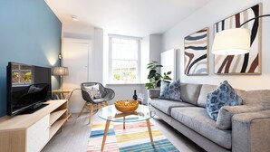 Ein modernes Wohnzimmer mit einer Couch, einem Glastisch, einem Fernseher und Kunstwerken an den Wänden.