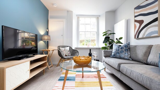 Ein modernes Wohnzimmer mit Flachbildfernseher, Glastisch, Sofa und großem Fenster.