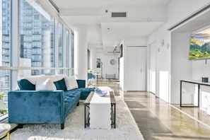 Ein modernes Wohnzimmer mit einem blauen Sofa, einem weißen Teppich und einem Essbereich mit Tisch und Stühlen.