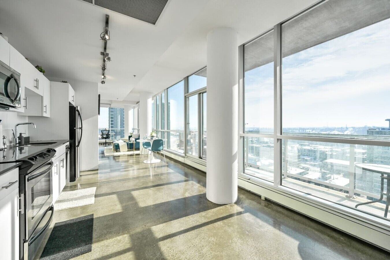 A modern kitchen with large windows, a dining area with chairs, and a view of the cityscape.