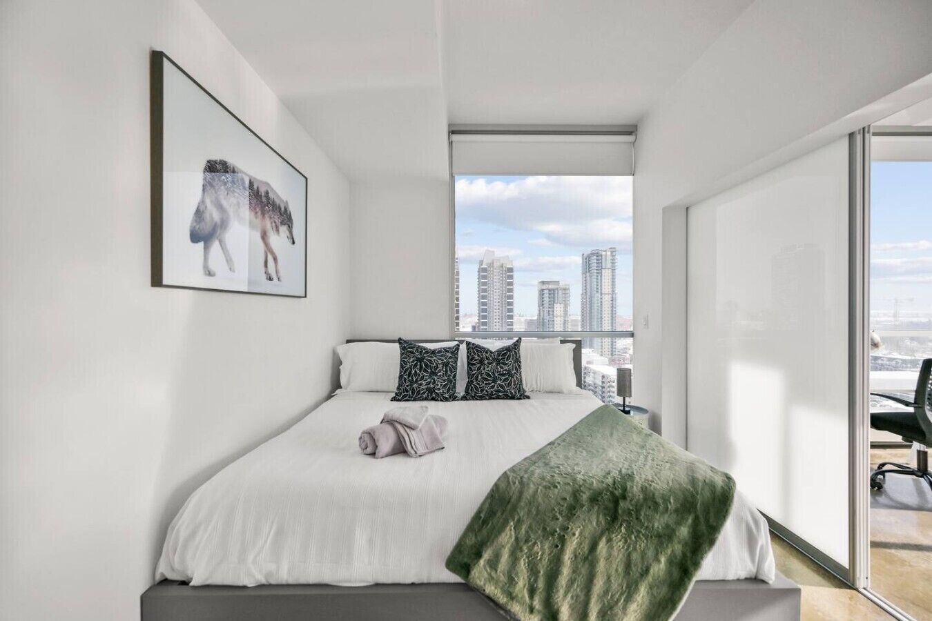 Une chambre moderne avec un grand lit, une vue sur la ville et un tableau encadré au mur.