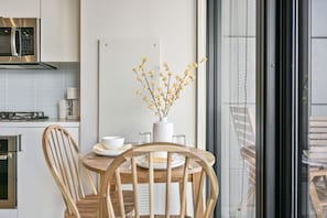 Ett modernt kök med ett matbord, stolar, en vas med blommor och utsikt genom en glasdörr.
