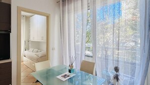 A modern bedroom with a glass table, a bed, and a view of the outdoors through sheer curtains.