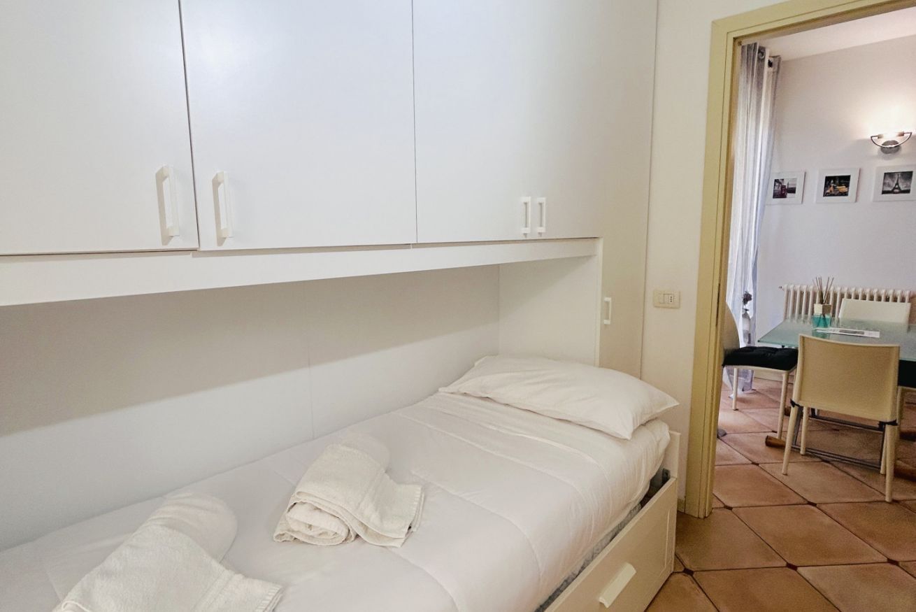 Een kleine kamer met een enkel bed, witte beddengoed en een eenvoudig, functioneel design.