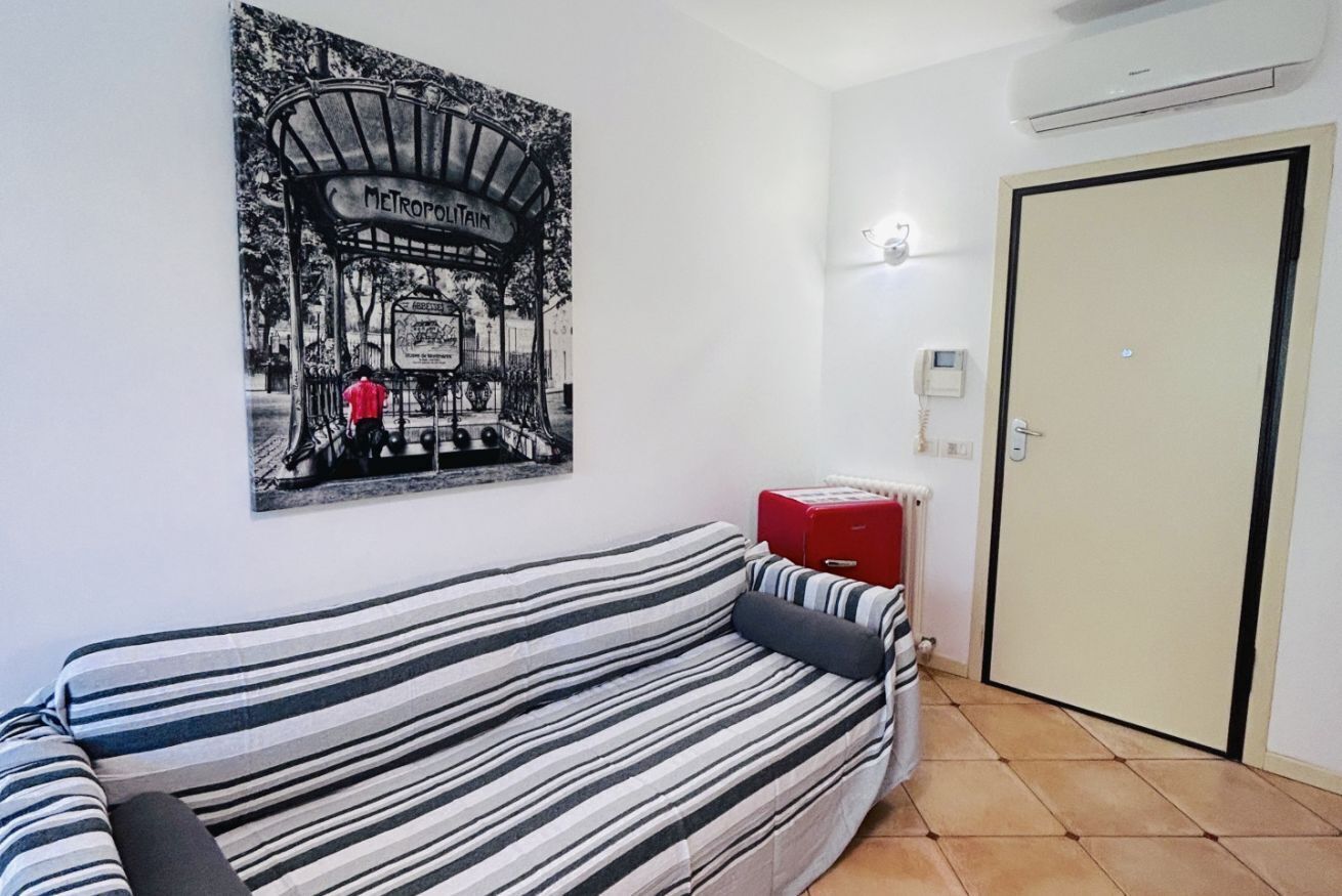 Une pièce avec un canapé à rayures, une affiche accrochée au mur, un radiateur et une porte.