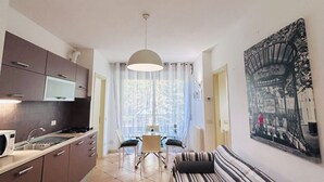 A modern kitchen with a dining area, a sofa, and a large window with curtains.