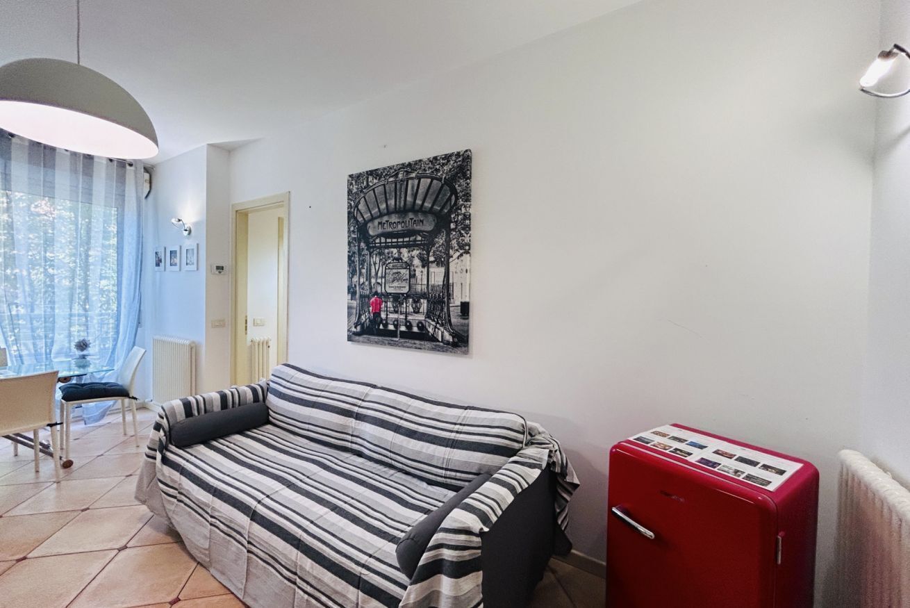 Een kamer met een gestreepte bank, een rode koelkast en een aan de muur hangend schilderij van een treinstation.