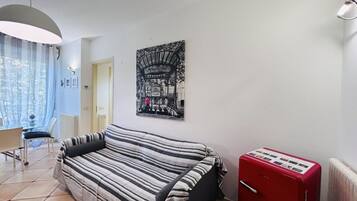 Een kamer met een gestreepte bank, een rode koelkast en een aan de muur hangend schilderij van een treinstation.
