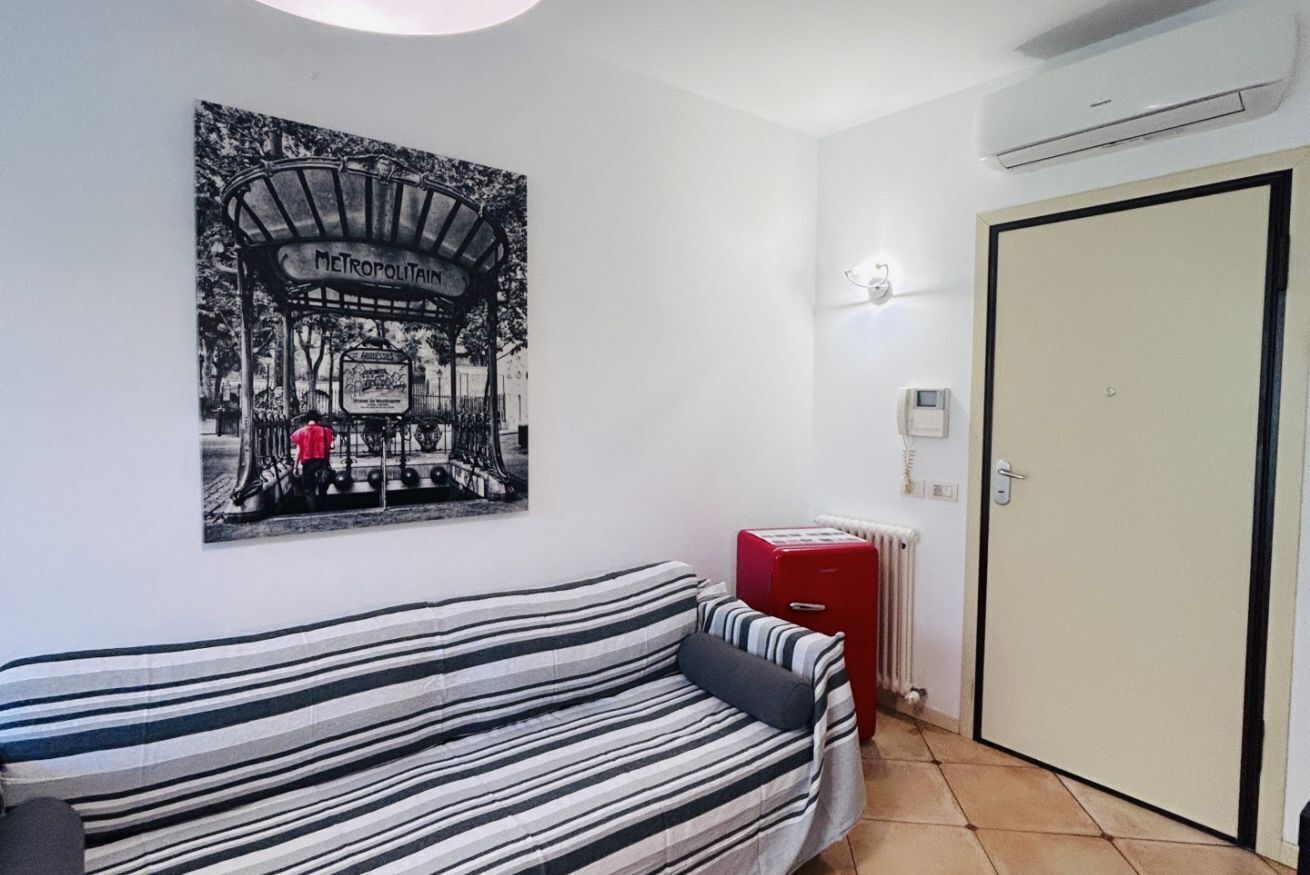 Um quarto com sofá listrado, um radiador, uma porta e uma luminária fixada na parede.