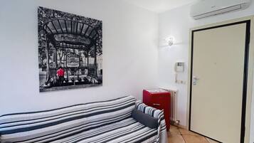 Um quarto com sofá listrado, um radiador, uma porta e uma luminária fixada na parede.