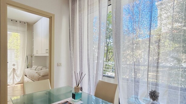 A room with a glass table, a bed, and a view of trees through sheer curtains.