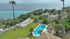 Ein Pool mit Blick auf das Meer, umgeben von Grünflächen und weißen Zäunen.