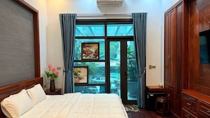 Une chambre à coucher avec un grand lit, une armoire en bois, une télévision et une vue sur un jardin, visible à travers une porte vitrée.