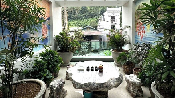 Un espace extérieur abrité, doté d’une table ronde entourée de grands bacs à plantes et de tabourets en pierre.