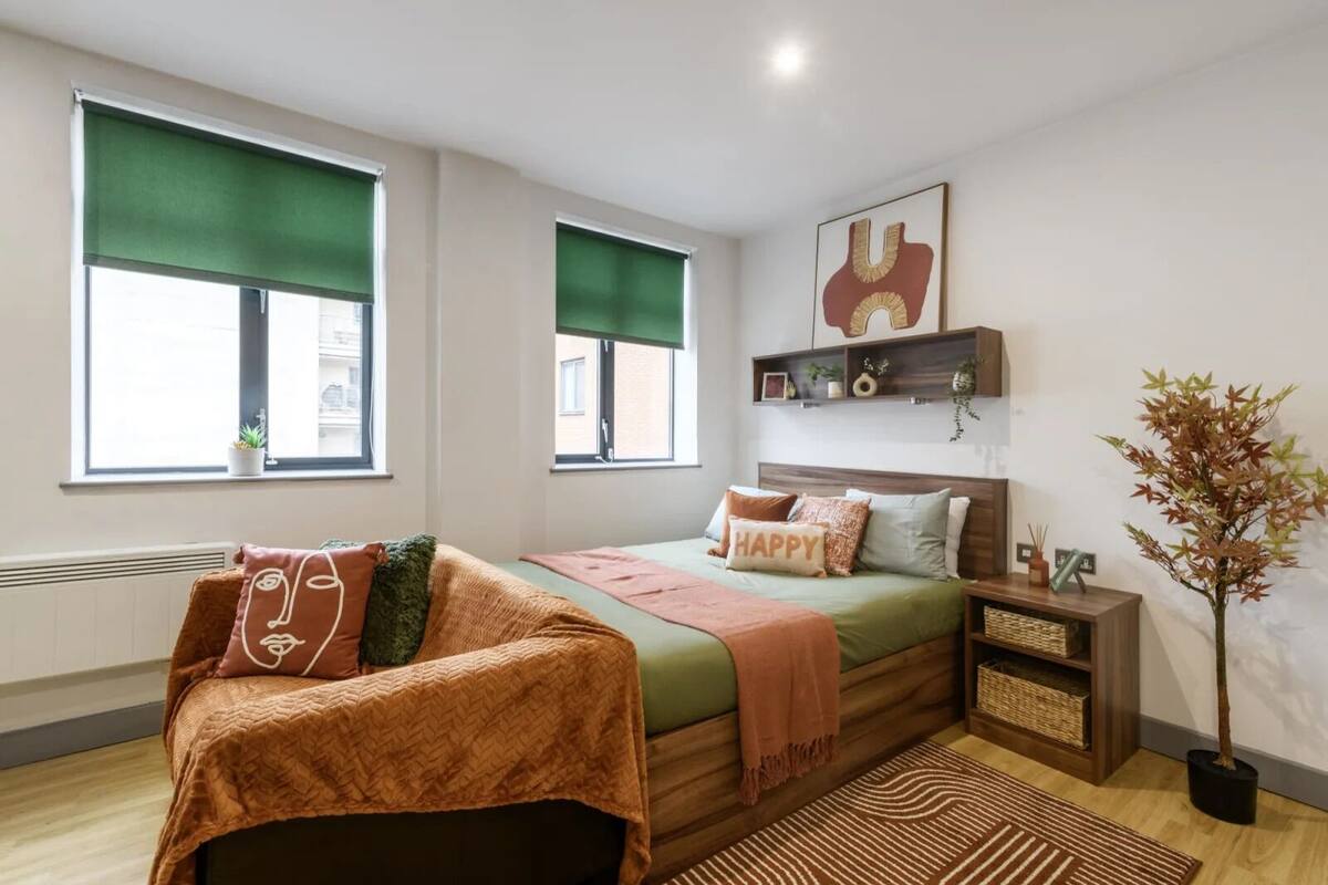 A bedroom with a bed, a sofa, a nightstand, a potted plant, and a window with a view.