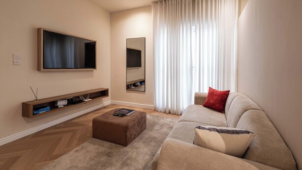A modern living room with a flat-screen TV, a large mirror, a beige sofa, and a wooden floor. - *NEW* Studio with King Size Bed in Lekki 1 (Lekki)