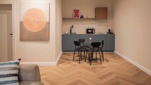 A modern kitchen with a dining area, featuring a large wall art, a wooden herringbone floor, and a small island with a sink and countertop. - *NEW* Studio with King Size Bed in Lekki 1 (Lekki)