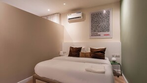 A neatly made bed with white bedding and brown pillows in a modern room with a green accent wall, a framed artwork above the bed, and a small bedside table with a lamp. - *NEW* Studio with King Size Bed in Lekki 1 (Lekki)