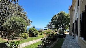 A courtyard with a stone pathway, potted plants, and a view of the sea. - Ground floor mansion for 6 people with swimming pool and jacuzzi (Bastia)