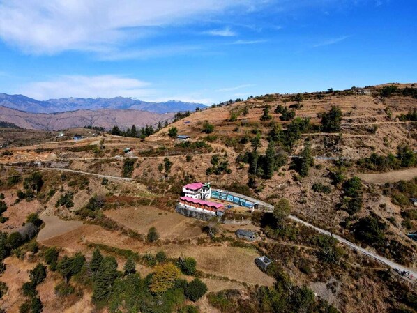 A remote, two-story building with a red roof, surrounded by dry, hilly terrain and sparse vegetation.