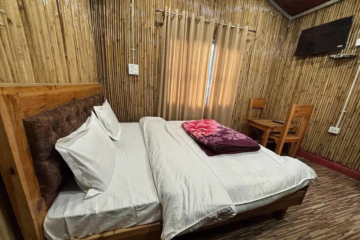 Een houten bed met witte en grijze lakens, een rood kussen en een houten hoofdbord.
