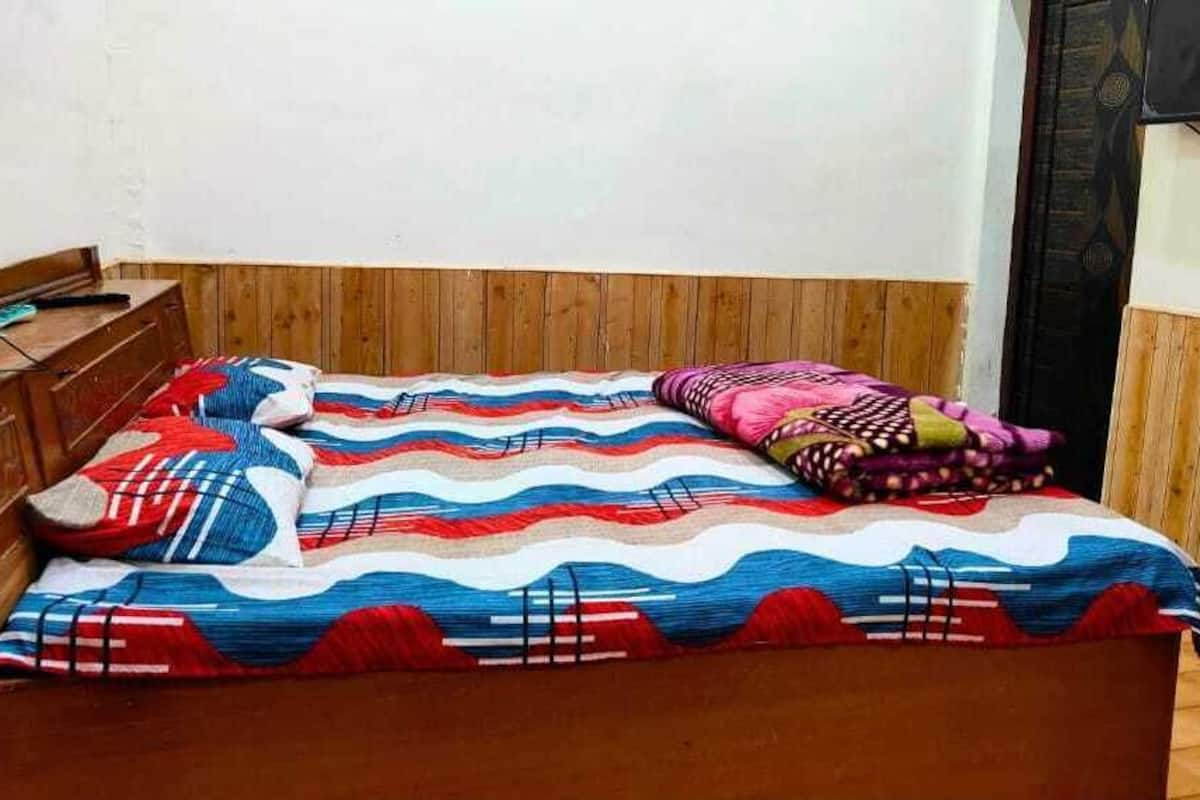 Een houten bed met een kleurrijke gestreepte dekbedovertrek en kussens, een houten nachtkastje en een televisie aan de muur.