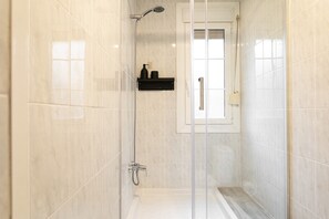 A walk-in shower with a glass door, tiled walls, and a small window. - Cozy Seaside Getaway in Barceloneta – Steps from the Beach! (Barcelona)