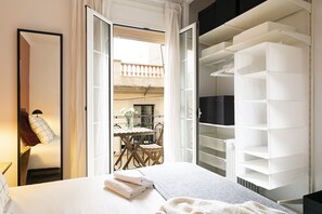 A bedroom with a bed, a bedside lamp, a mirror, and a view of a balcony with outdoor furniture. - Cozy Seaside Getaway in Barceloneta – Steps from the Beach! (Barcelona)