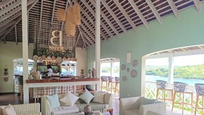 Un vaste espace de détente avec des meubles en osier, un bar offrant une vue panoramique et un plafond orné de poutres en bois.