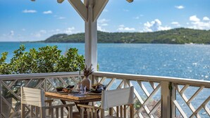 Une terrasse en bois avec une table dressée pour le repas, offrant une vue sur une étendue d’eau et des collines verdoyantes.